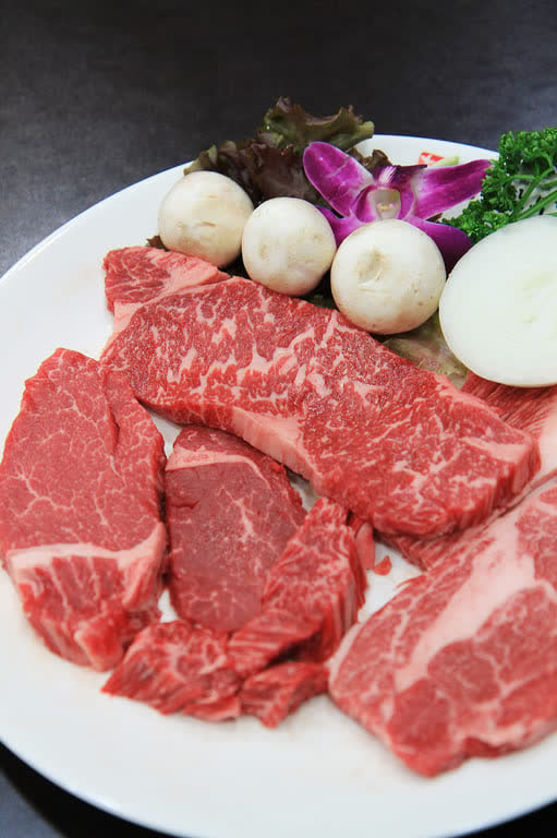 A plate of raw hanwoo cuts with dense white marbling, next to mushrooms and onion
