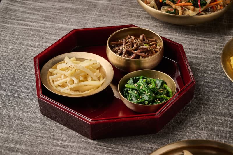 Three brass bowls of namul side dishes, bellflower root, fernbrake and spinach, on a lacquered octagonal tray