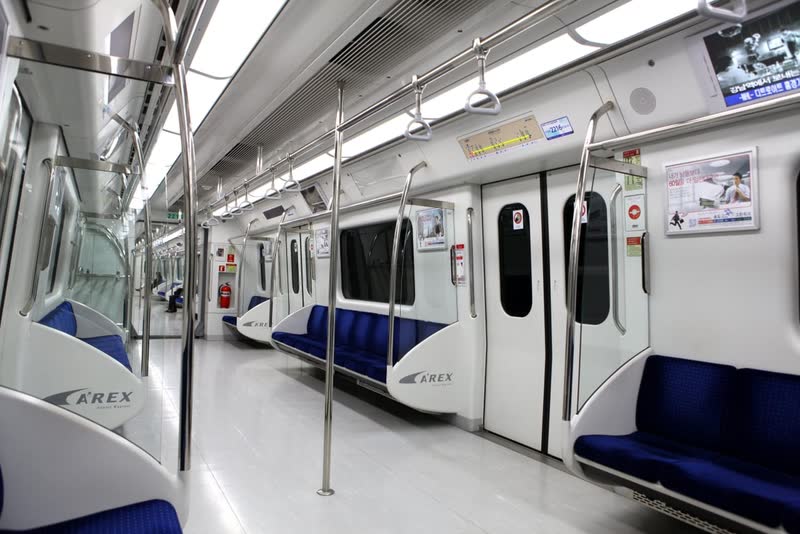 Inside an AREX airport railroad train car with long side benches and handrails