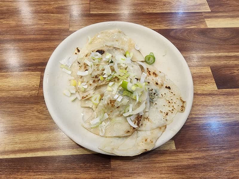 Plate of griddled napjak-mandu, Daegu's flat dumplings, topped with chopped green onion