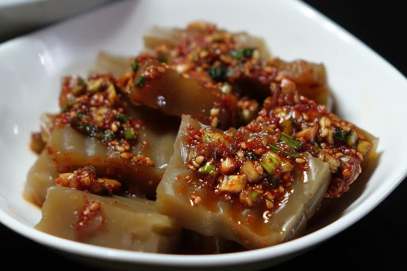 Cubes of brown acorn jelly dressed with chopped chili, green onion and sesame in a white bowl