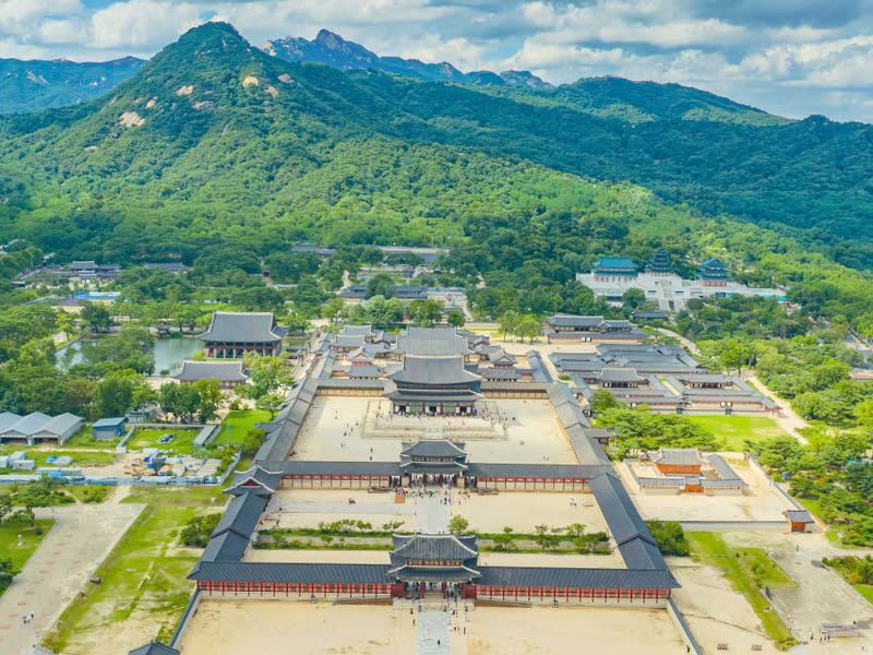 Aerial view of Gyeongbokgung Palace with forested Bugaksan behind it and Bukhansan's rocky peaks on the skyline
