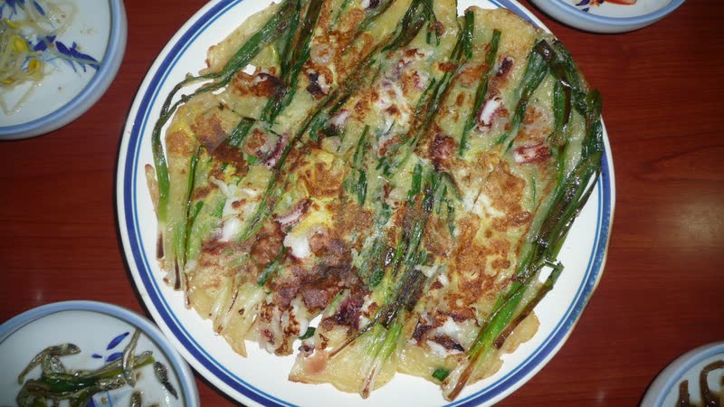 A large green-onion pancake with seafood on a white plate with a blue rim