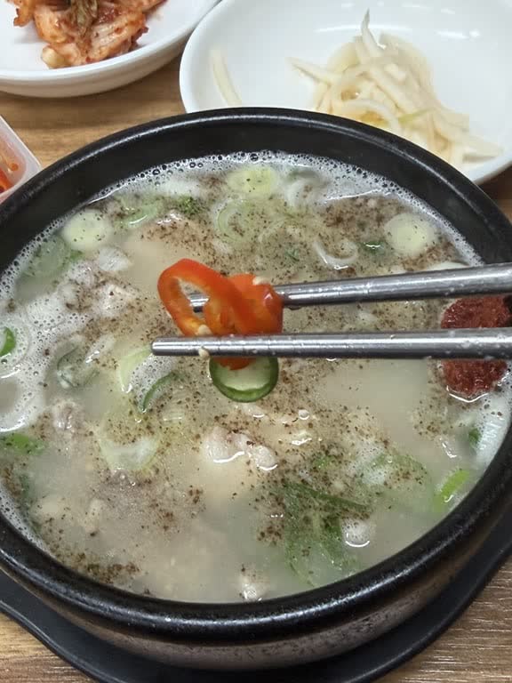 Chopsticks holding slices of red and green Cheongyang chili over the soup