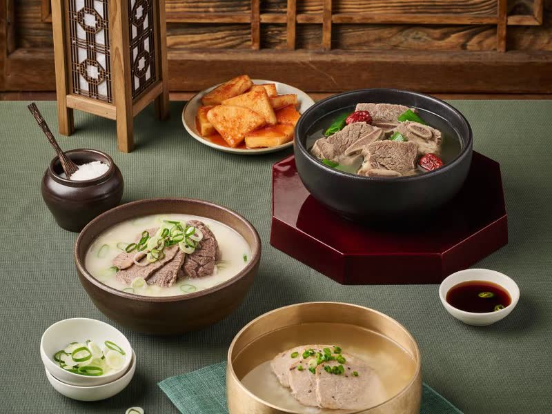 Bowls of gukbap, beef soup with rice, with kimchi and small side dishes on a table