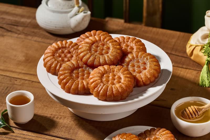 Flower-shaped yakgwa honey cookies stacked on a white cake stand, with a small dish of honey and a cup of tea