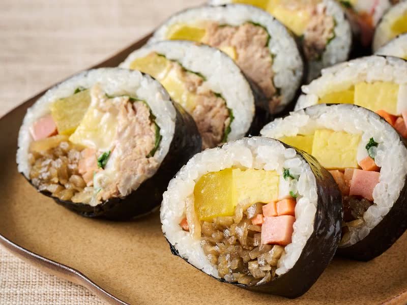 Sliced gimbap rolls with tuna, egg, pickled radish and ham filling on a brown plate