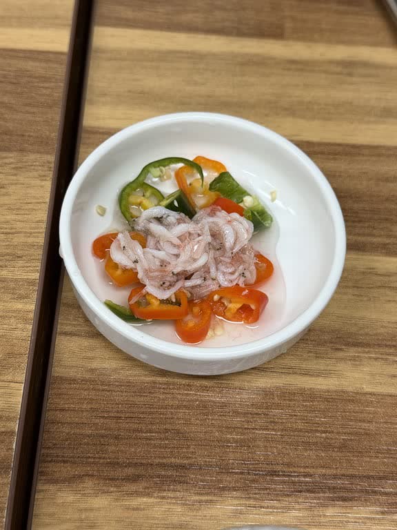 A small white dish of salted tiny shrimp with sliced red and green chilies