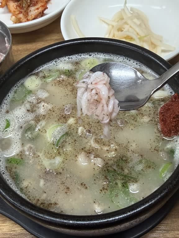 A spoon of salted tiny shrimp being lowered into a bowl of sundae gukbap