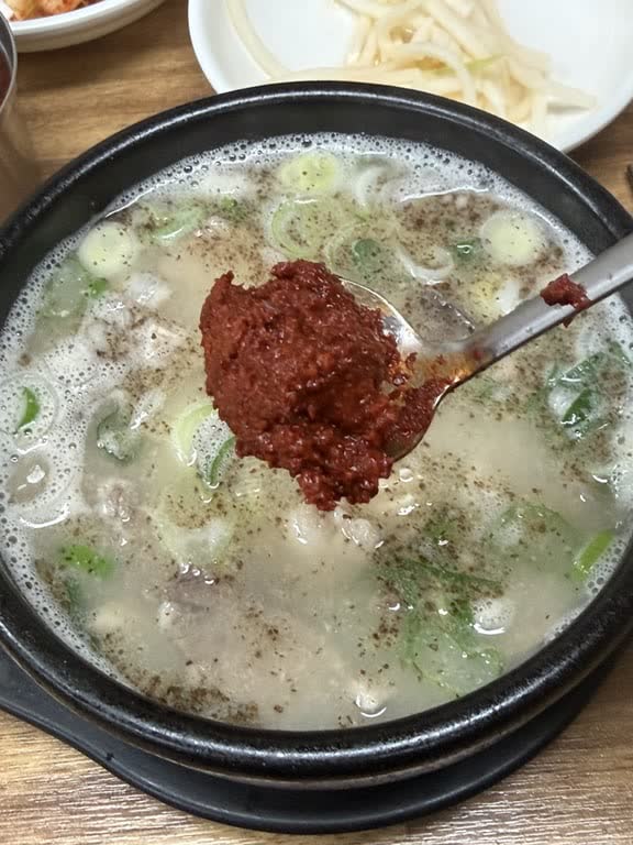 A spoonful of red dadaegi seasoning paste held over a bowl of milky pork soup