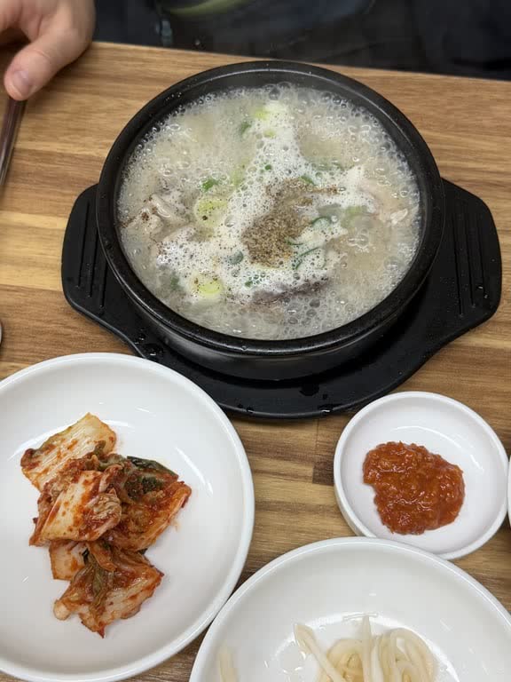 A bubbling bowl of sundae gukbap with a heap of perilla seed powder on top, next to kimchi and a dish of red seasoning paste
